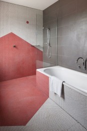 a contemporary bathroom with red geometric detailing, white penny tiles and large scale grey ones is very stylish and bold
