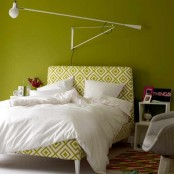 a pistachio green bedroom with a matching printed bed and neutral bedding, a grey chair and mismatching nightstands and a simple white sconce