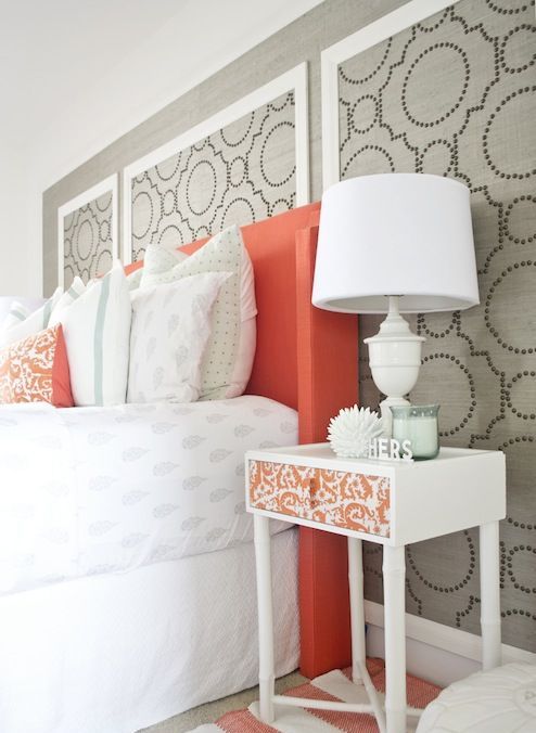 a cheerful grey, white and coral bedroom with a printed wall, a coral bed, bright textiles and a cool white and coral nightstand