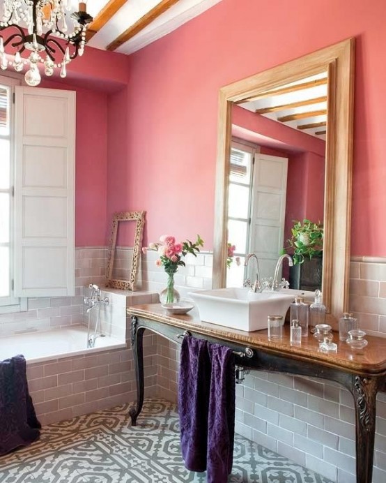 a chic bathroom with a grey floor and walls, coral paint, a large mirror and a crystal chandelier plus a vintage table console