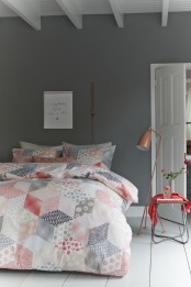 a grey and white bedroom, a small side table with a coral cover, grey, white and coral bedding with a print and a copper lamp