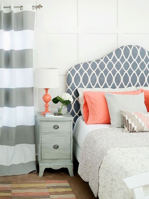 an eclectic bedroom with striped curtains, a printed bed, coral and pink pillows and a whitewashed nightstand