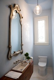 a pastel blue guest toilet with a large wooden vanity, a mirror in a vintage frame and a pendant lamp