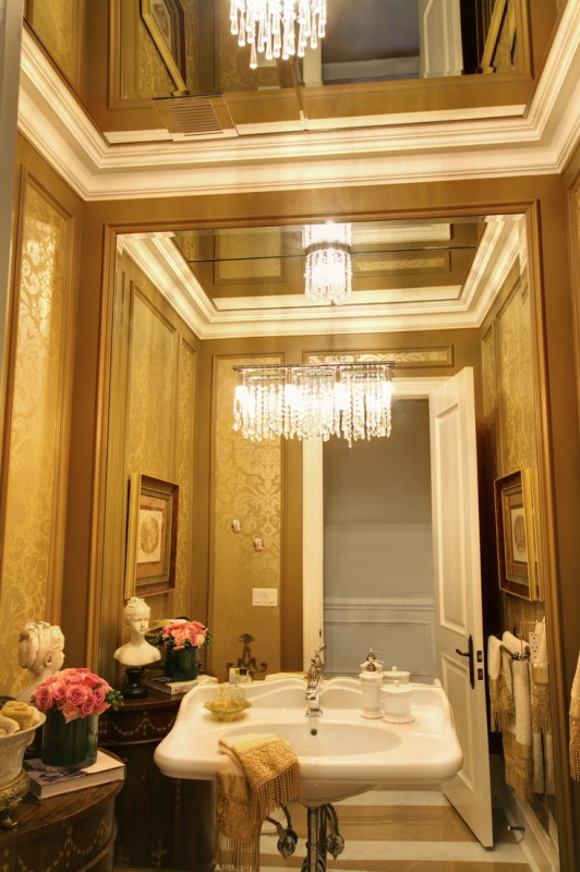 a chic refined guest toilet with neutral and gold printed wallpaper, a mirror wall and a wall-mounted sink