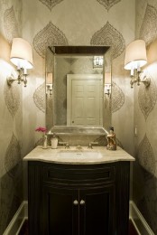 a small neutral guest toilet with printed wallpaper, a dark vanity, a mirror and wall lamps