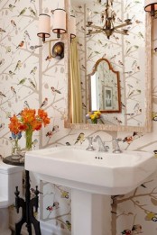 a cheerful guest toilet with a free-standing sink, floral and bird print wallpaper, wall lamps and a framed mirror