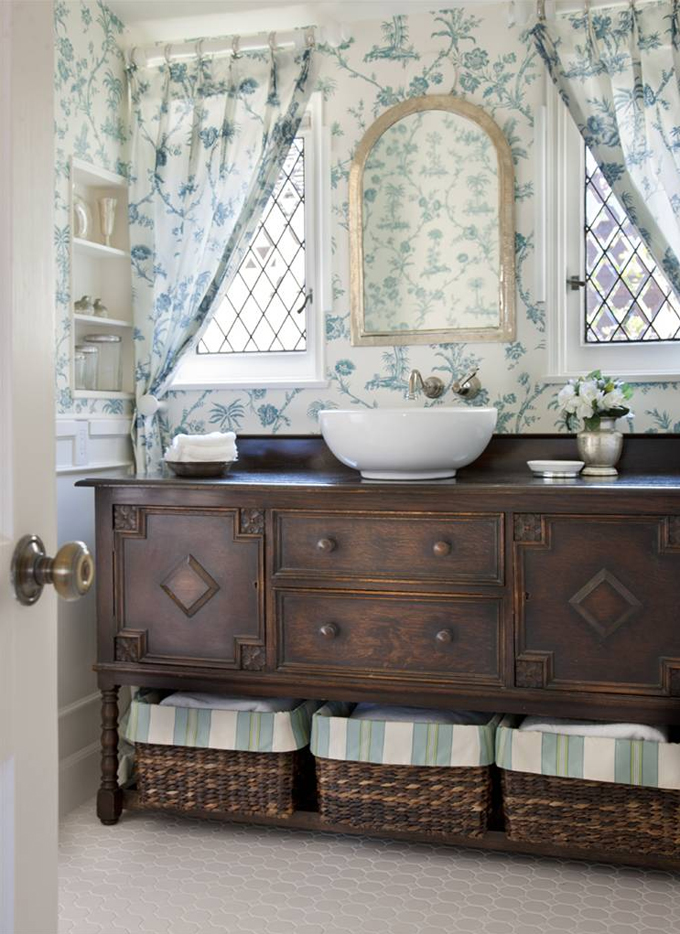 a neutral and elegant guest toilet with a vntage dark stained vanity, a vessel sink, a mirror and floral print curtains