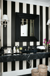 a striped black and white guest toilet with a black framed sink, a stone vanity, wall lamps and baskets