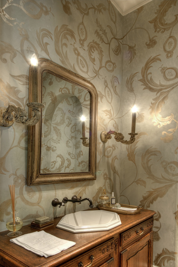 a refined and chic guest toilet with printed wallpaper, a framed mirror, a wooden vanity and wall lamps