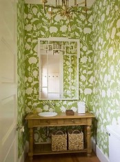 a guest toilet done with green printed wallpaper, a wooden vanity, a chandelier and a mirror