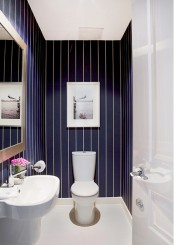 a small guest toilet with navy and white thin stripe wallpaper, a white wall-mounted sink and an artwork