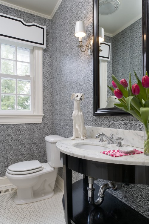 a refined guest toilet with printed wallpaper, a black vanity with a stone countertop and a large mirror in a dark frame