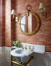 red printed wallpaper, a mirror in an elegant vintage frame, wall lamps and a round sink