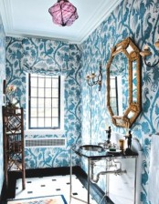a bright guest toilet done with teal botanical print wallpaper, a delicate vanity with a sink, an exquisite mirror and a storage unit