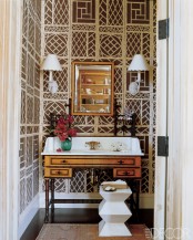 an eclectic toilet with geometric print wallpaper, a vintage wooden vanity, wall lamps