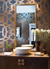 a refined guest toilet with printed wallpaper, a wooden vanity with a vessel sink, wall lamps