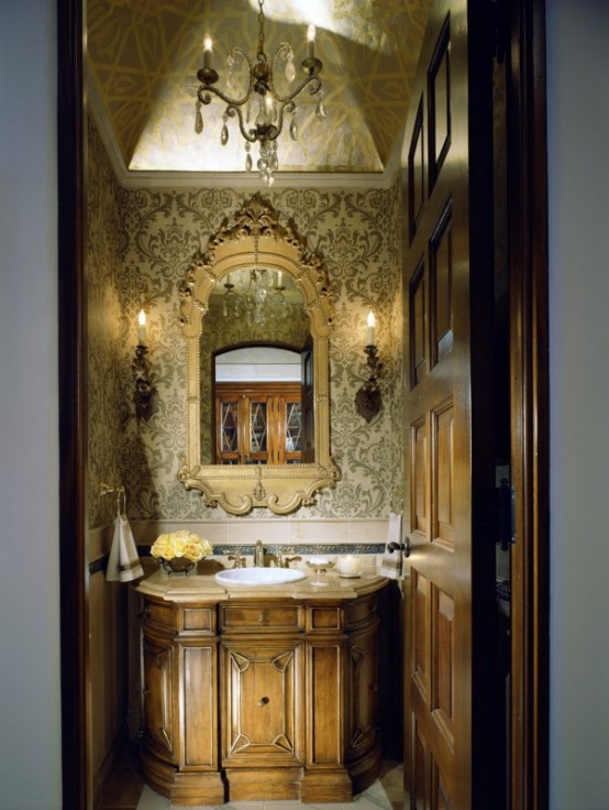 an elegant and exquisite powder room with refined print wallpaper, a chic mirror in a frame, a wooden vanity and some candle-like lamps