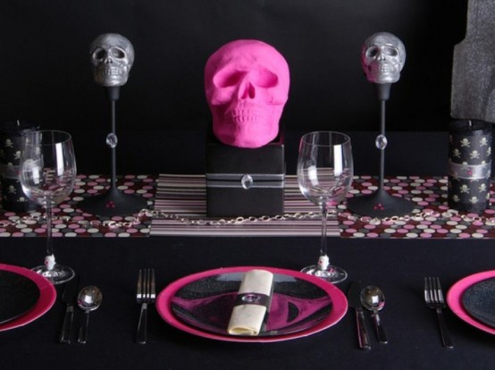 a modern black and pink Halloween tablescape with black and pink plates, a polka dot runner, stands with pink and grey skulls, black cultery is all cool