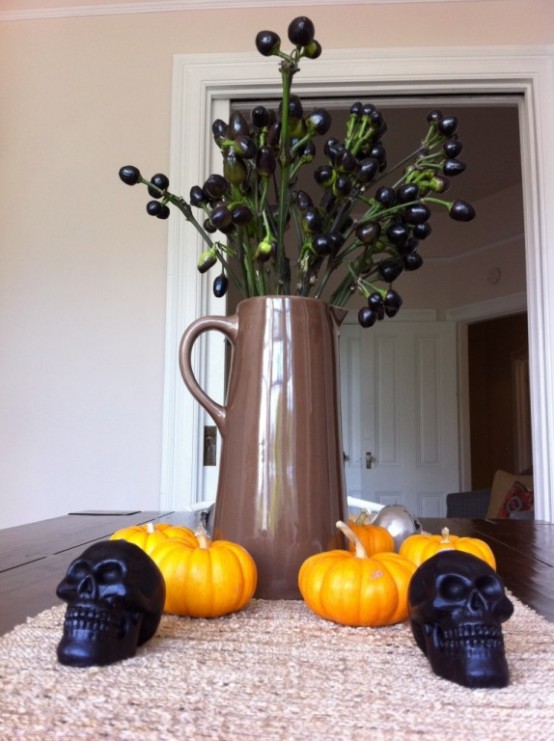 a Halloween centerpiece of a jug with black berries, orange pumpkins and black candles is a simple to reliaze idea you can go for