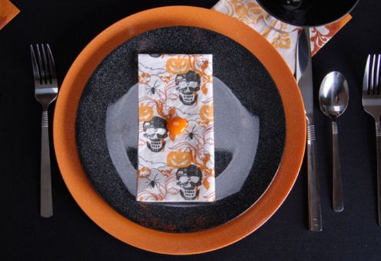 a contrasting black and orange place setting with an orange charger and a black plate, a colorful printed napkin and black cutlery