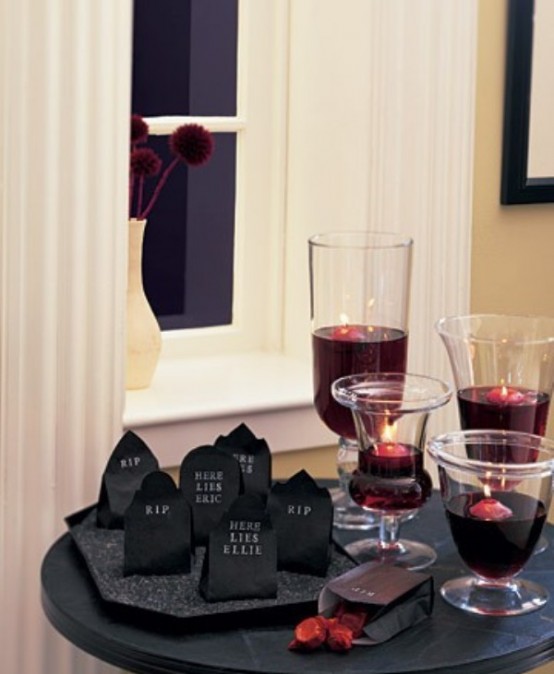 a chic table with glasses with blood and floating candles, black paper bags with favors is a lovely idea for a Halloween party