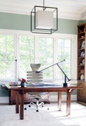 an eye-catchy mid-century modern home office with a stained desk, a neutral chair, a stained storage unit, a black lamp and a catchy pendant lamp
