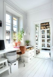 an airy Scandinavian home office with a windowsill desk, a ladder and boxes for storage, a wall sconce and some greenery