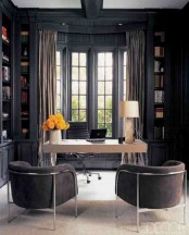 a sophisticated moody home office with black walls and built-in bookcases, a light-stained and sleek desk, brown chairs and a cool bay window