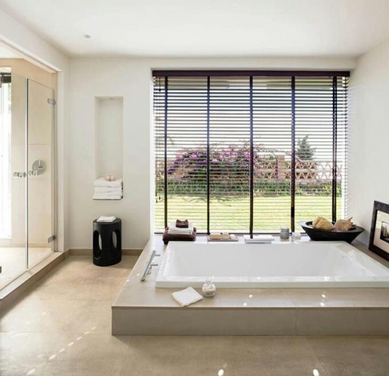 a contemporary neutral bathroom with a shower space, a large hot tub, a large window with blinds, black stools and bowls and some artwork