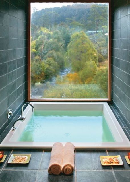 a small home space clad with grey tiles, with a square tub and a large window to enjoy the views will provide full relaxation