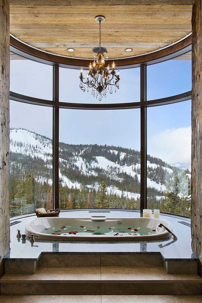 a gorgeous home space with a curved window, a fantastic mountain view, a built in tub and a crystal chandelier