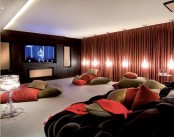 a contrasting living room with a built-in screen, red curtains, catchy pendant lamps, a black sofa and piles of colorful pillows