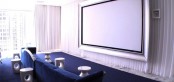 a stylish home theater with a large screen, a glazed wall that can be hidden with curtains and a navy floor and matching navy furniture