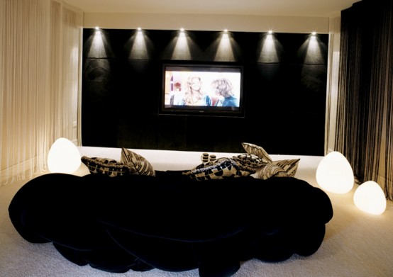 a contrasting home theater nook with a black accent wall, a screen, lots of lights around and a black sofa plus printed pillows