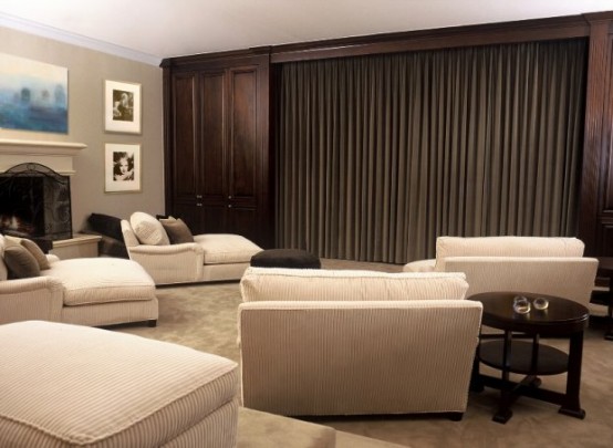 a chic and cool home theater with a large screen hidden with a curtain, white seating furniture, a fireplace and a gallery wall is cool and great