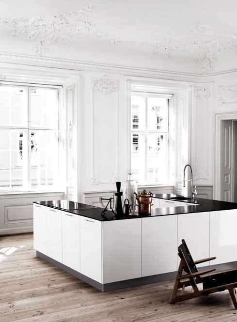 a beautiful Scandinavian kitchen with a refined ceiling with stucco,modern white cabinets and black countertops, a dark stained chair and lots of natural light incoming