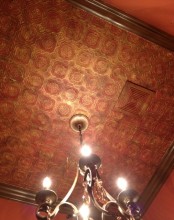 a beautiful red ceiling with red and gold tin tiles, a frame around and a heavy chandelier for a refined and bold space