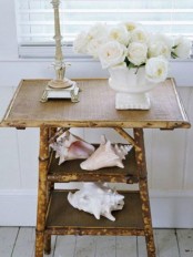 a rustic console table covered with burlap and with large shells and white blooms for beachy decor
