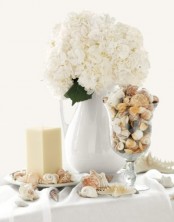 seashells in a tall glass and all around on the table plus white hydrangeas look very chic and feel nautical