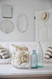a round jar filled with starfish and seashells plus some bottles for decorating a whitewashed beach and coastal space