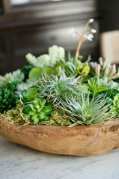 a wooden bowl with moss, hay and succulents plus some blooms is a stylish centerpiece with a strong natural feel