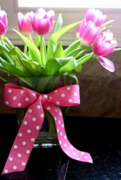 a clear vase with bright pink tulips and a hot pink polka dot bow on the vase for adding a cheerful touch to the space