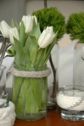 a clear glass jar with white tulips and rope wrapping the jar is a simple rustic decoration or centerpiece