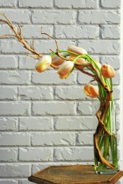 a clear glass vase with orange tulips and vining branches is a bold spring decoration or centerpiece with an unusual ikebana-inspired shape