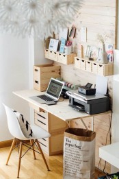 a wooden wall-mounted storage unit with some holders and little wooden drawers that hold pencils and pens