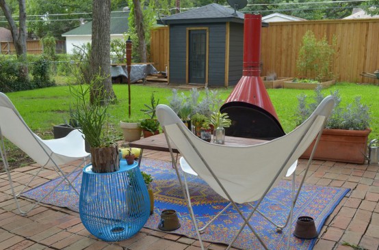 an outdoor living room with a red Malm fireplace, white butterfly chairs, a blue side table and a blue printed rug is a lovely nook to enjoy fresh air
