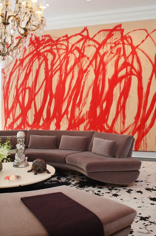 a refined living room with a bold red graffiti wall that stands out and taupe seating furniture and a crystal chandelier