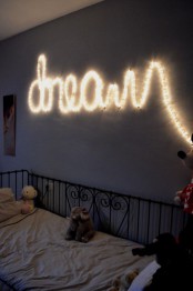 a small kid’s room with a grey wall, a black metal bed with neutral bedding, a string light that is forming a word on the wall that serves as a light source and a decoration at the same time