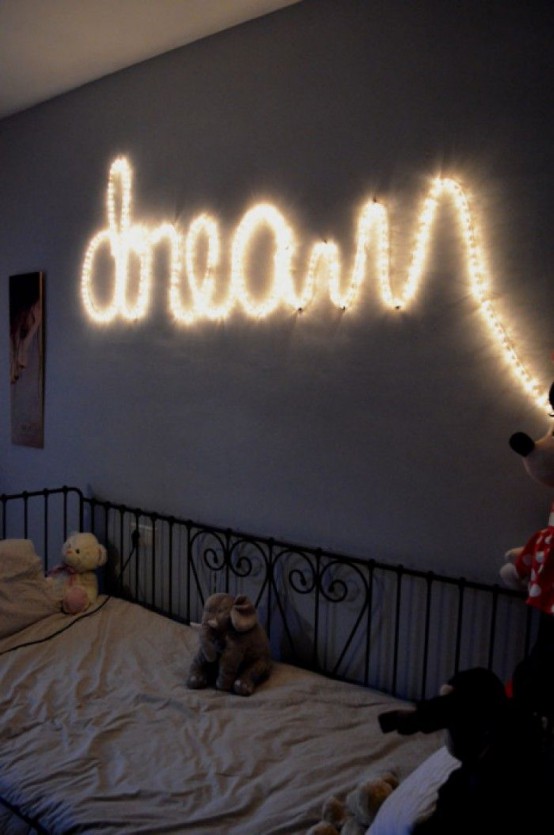 a small kid's room with a grey wall, a black metal bed with neutral bedding, a string light that is forming a word on the wall that serves as a light source and a decoration at the same time