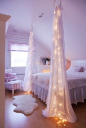 an airy attic bedroom with a bed with neutral bedding, curtains and lights inside them that add light to the space and make it mmore eye-catchy
